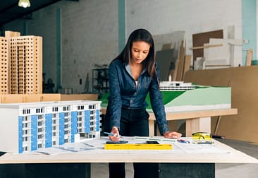 Serious-African-american-lady-with-pen-standing-near-model-of-building-on-table Lady Selling Commercial Properties